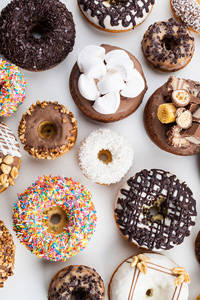 Assorted gourmet donuts with various toppings including sprinkles, nuts, chocolate icing, and marshmallows on a white background.