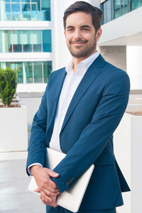 Confident businessman in smart casual attire holding a laptop standing outside a modern office building