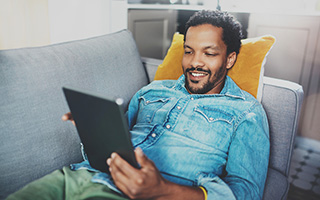 male student sitting on a couch using a tablet
