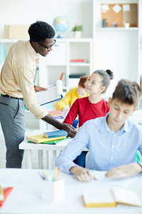 A teacher pointing something out to a student in the second row of a classroom