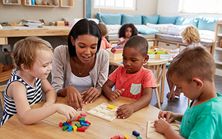 A teacher and three young students working through a colorful puzzle on a classroom table