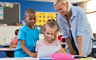 A teacher and two young students gathered around an open laptop at a classroom desk