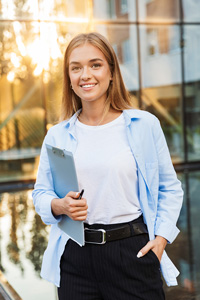 Smiling young professional woman holding a tablet outdoors with a modern building in the background